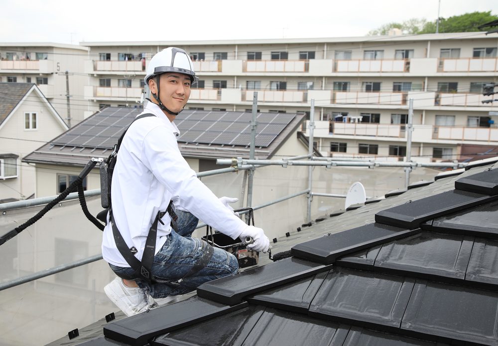屋根の上で塗装する当社の職人。棟板金の状態もこのとき確認します